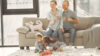 Cheerful family smiling while spending weekend together sitting parents sitting on comfortable sofa while children resting on carpet and playing